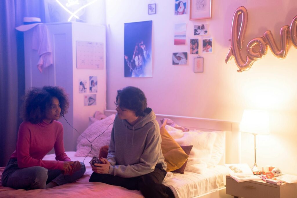 Two teenagers sharing a music player in a cozy bedroom with warm lighting.