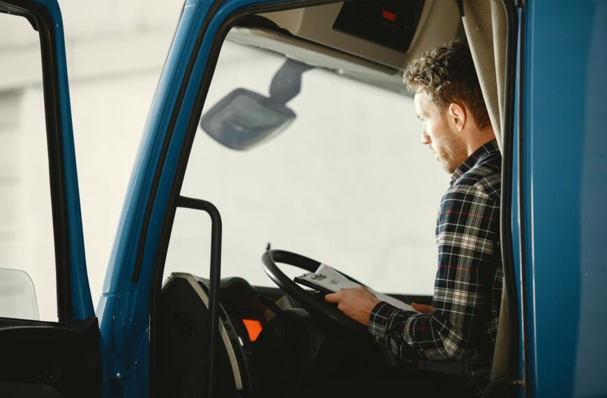 A man sitting in a truck cabin reading a document inside a blue truck, showcasing focused driving preparation.
