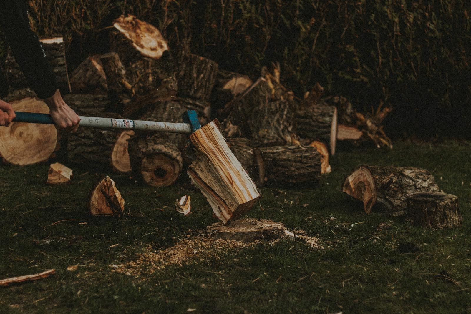 Unrecognizable male worker chopping firewood with ax on grassy lawn near pile of fried logs in suburb area of countryside