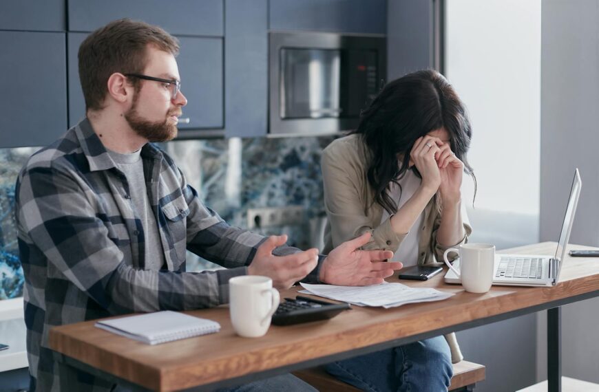 A couple seated at a table, looking stressed while discussing financial issues indoors.