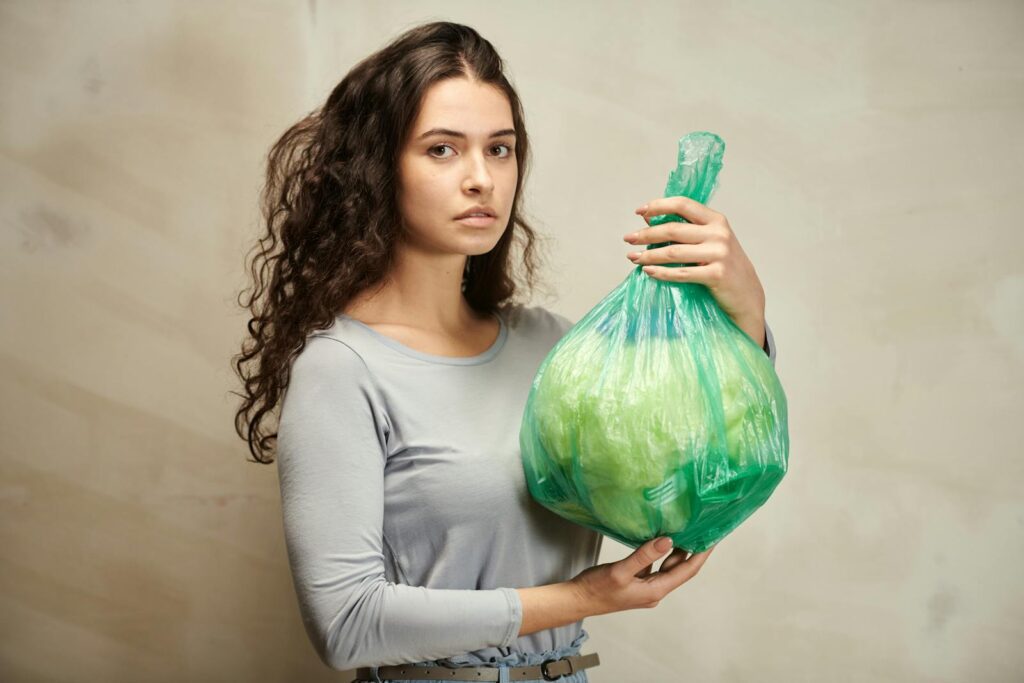 Portrait of a young Caucasian woman holding a green plastic bag filled with vegetables.