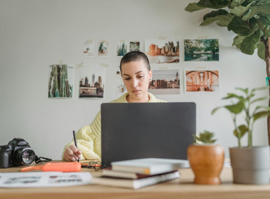 Professional female designer looking at laptop and using graphic tablet while sitting at table in light workspace