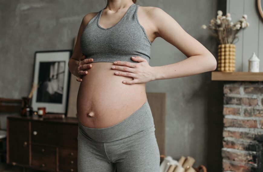 Pregnant woman in activewear enjoys wellness indoors, holding baby bump in a cozy setting.
