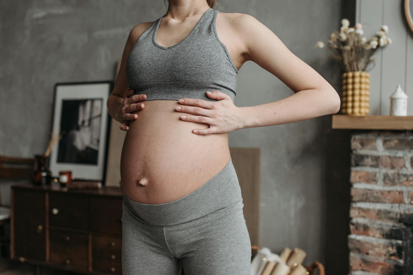 Pregnant woman in activewear enjoys wellness indoors, holding baby bump in a cozy setting.