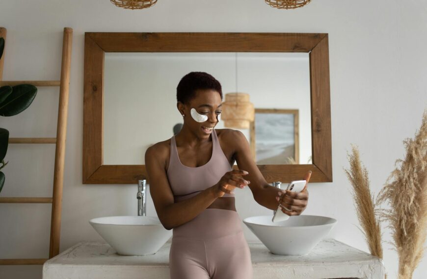 Young woman smiling in a bathroom while using skincare patches and video calling on phone.