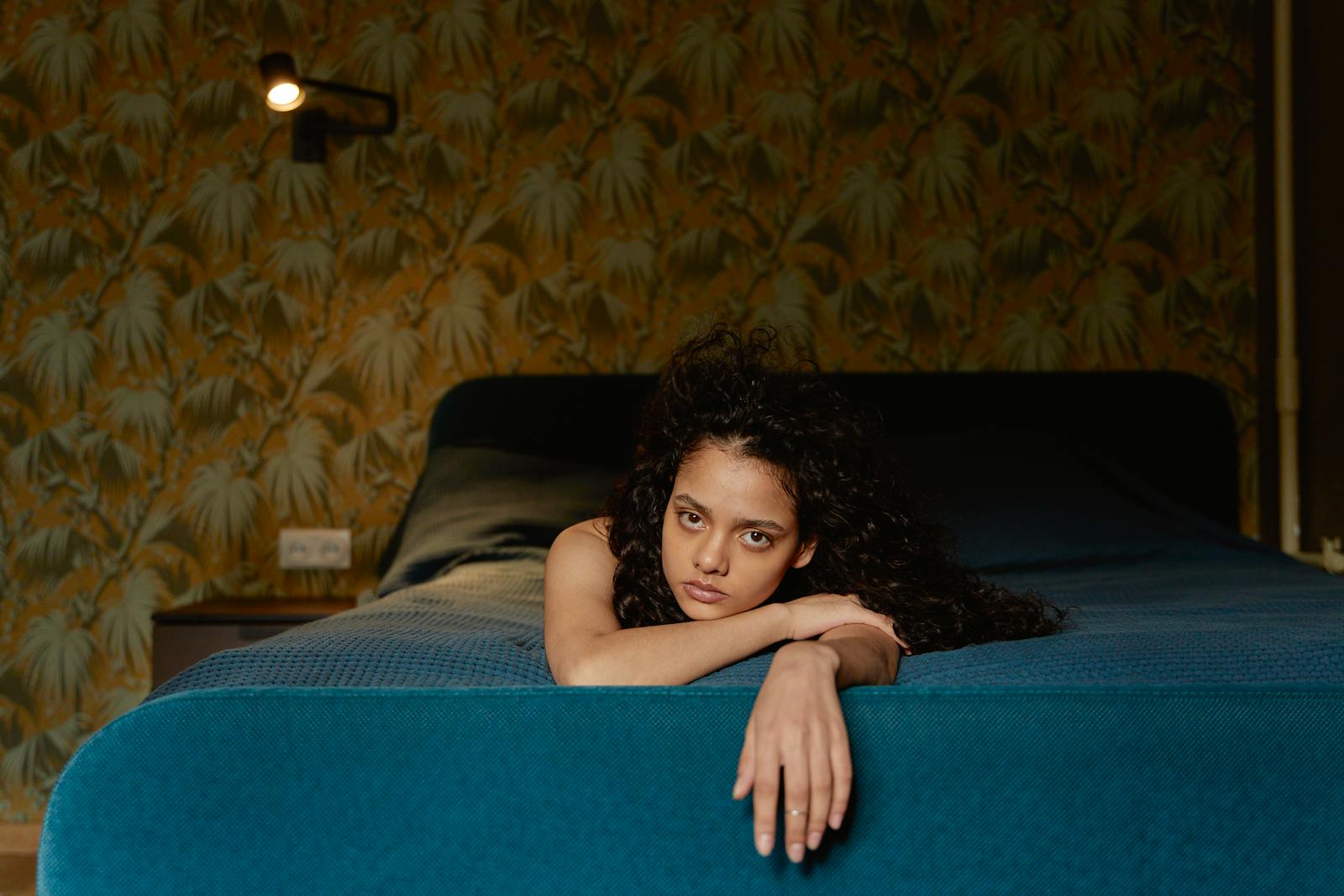 Portrait of a young woman lying on a bed with a pensive expression, indoors.