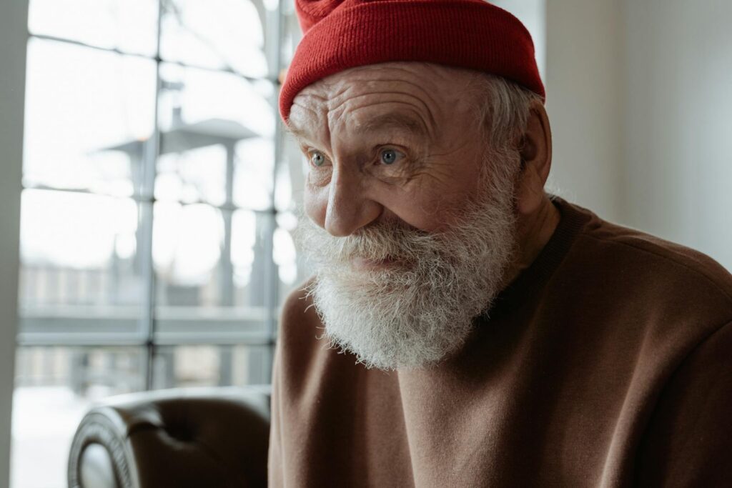 Charming portrait of an elderly man smiling with a red beanie, indoors.