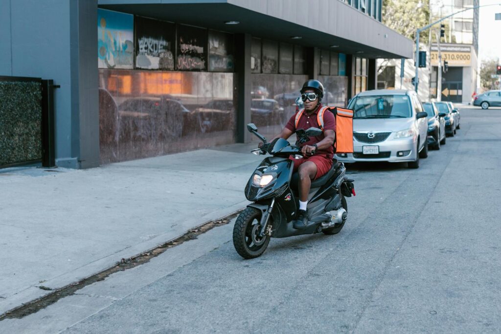 African American man delivering on a scooter in the city wearing safety gear.