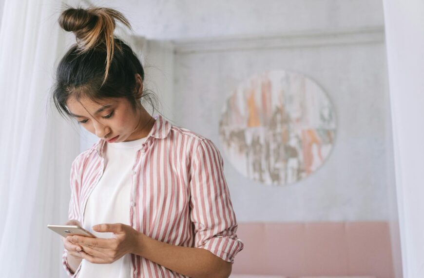 A young woman in a striped shirt using her smartphone indoors with soft decor and a relaxed atmosphere.