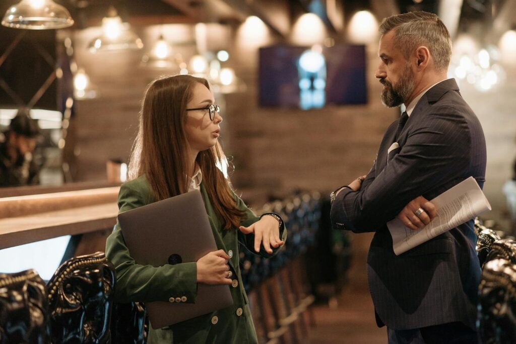 Two business professionals engaging in conversation in a stylish bar interior, highlighting modern work culture.
