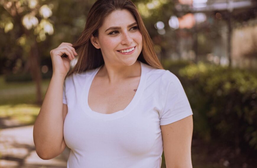A woman smiles while posing in a white shirt outdoors during the day.