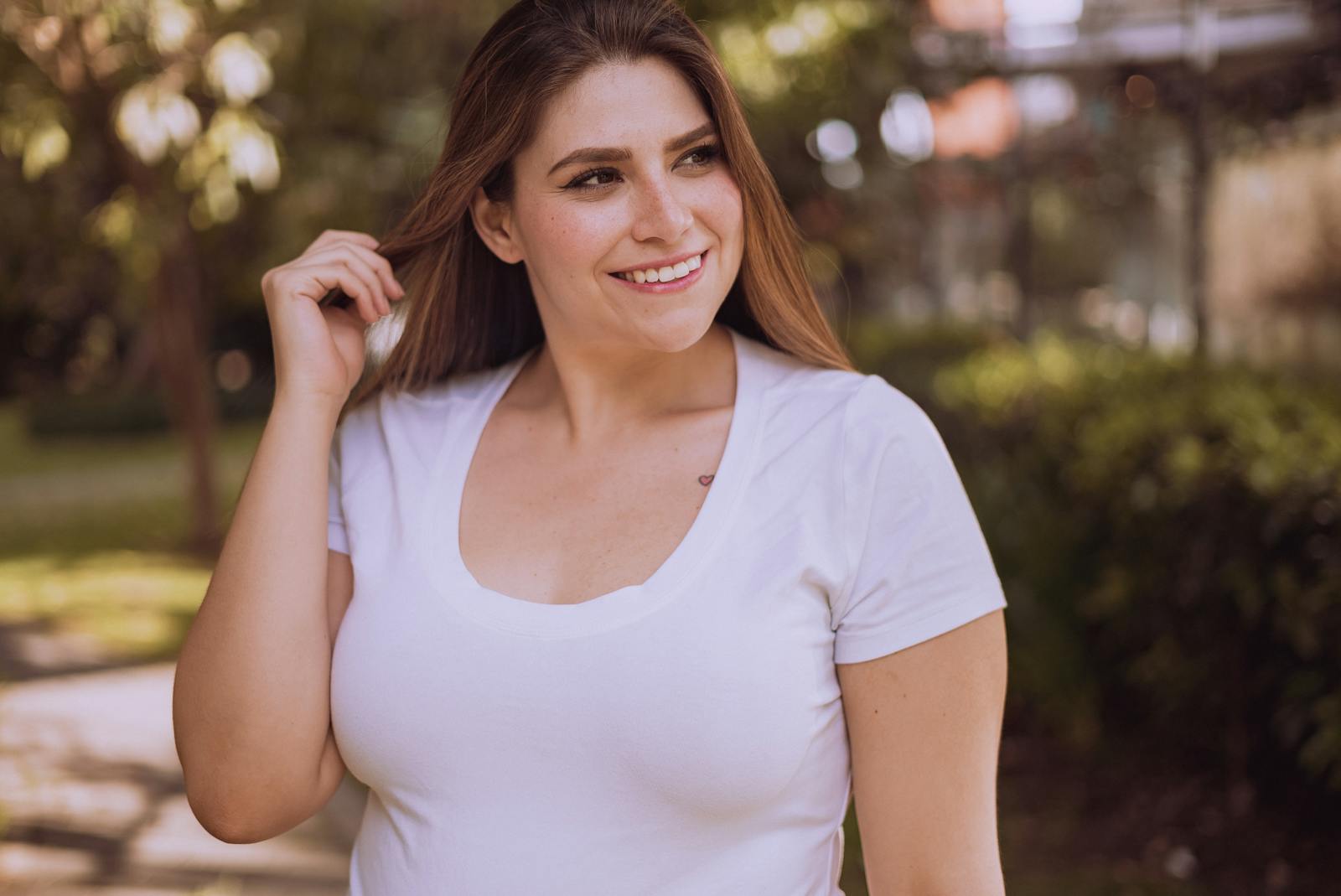 A woman smiles while posing in a white shirt outdoors during the day.