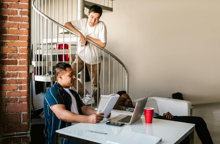 Young adults in an urban apartment discussing study materials around a spiral staircase.