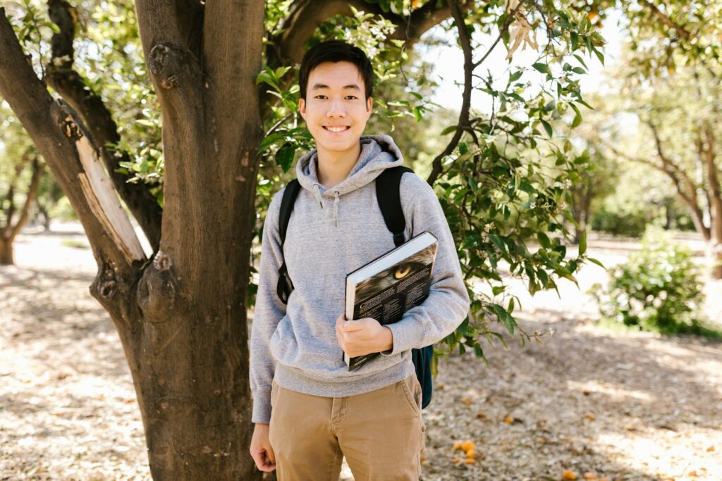Young college student standing outside holding books, smiling at the camera.