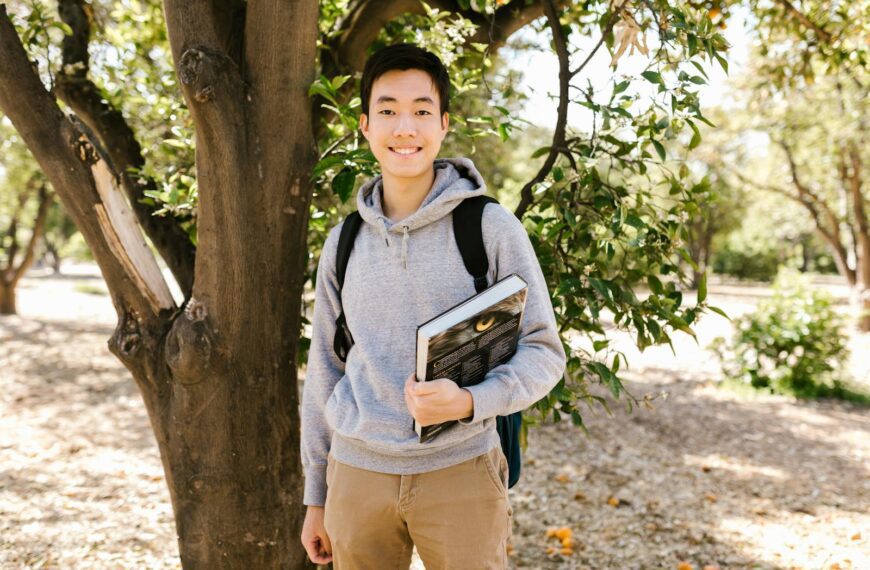 Young college student standing outside holding books, smiling at the camera.