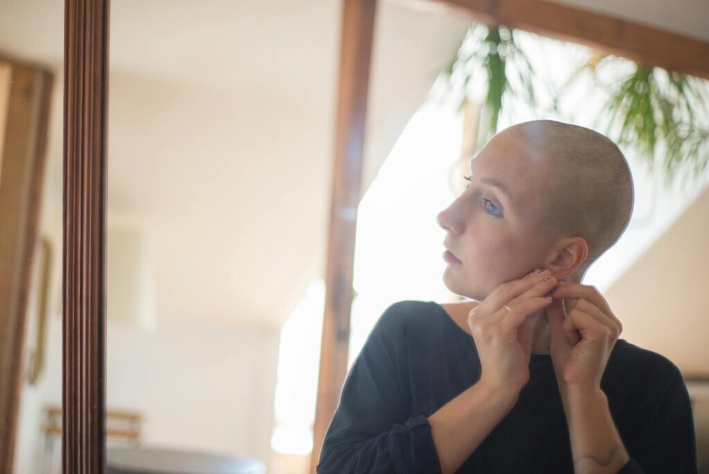 Bald woman wearing earring in front of mirror, serene expression.