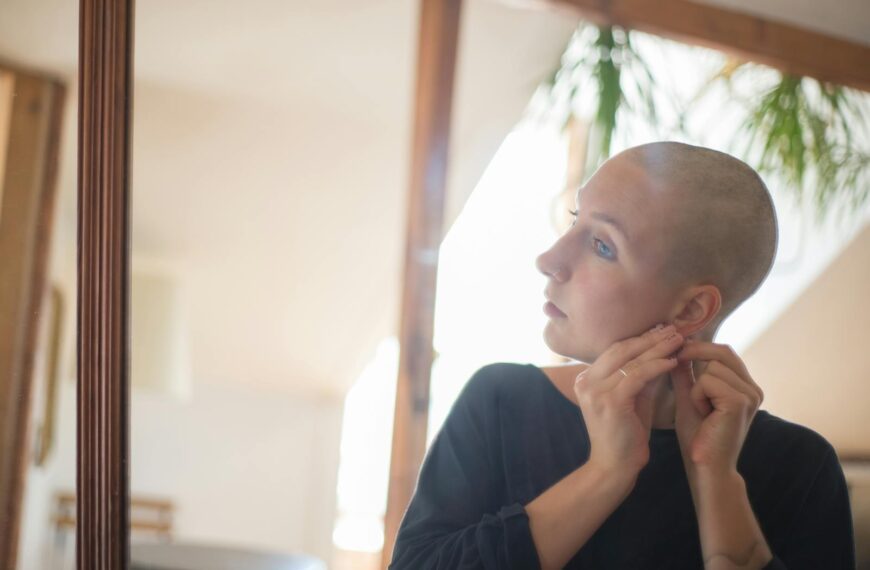 Bald woman wearing earring in front of mirror, serene expression.