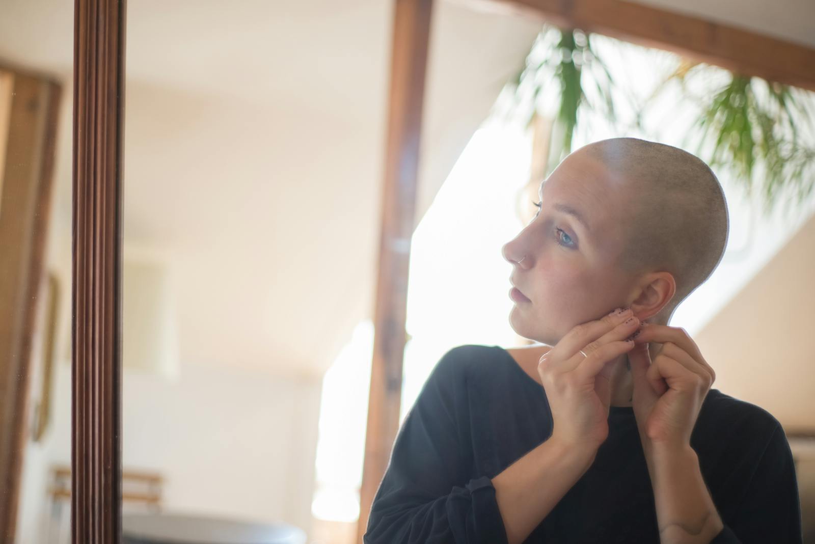Bald woman wearing earring in front of mirror, serene expression.