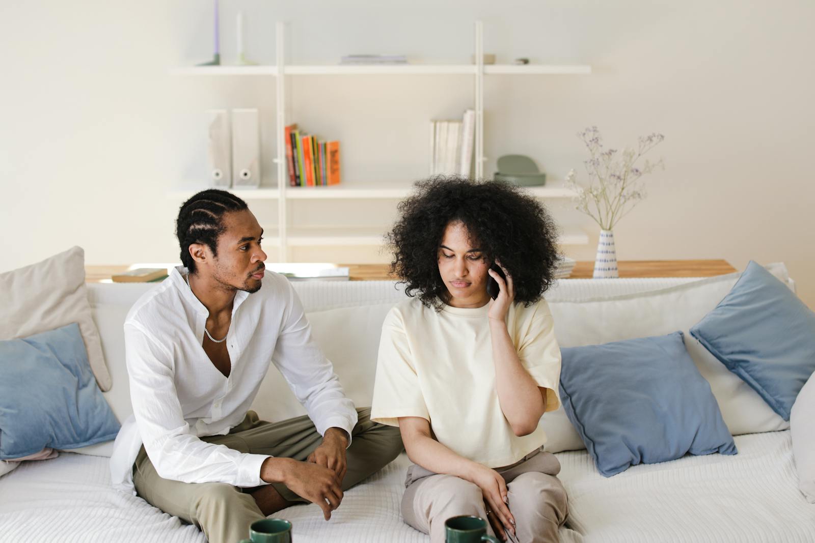 African American couple relaxing at home, sitting on sofa, talking and using phone.