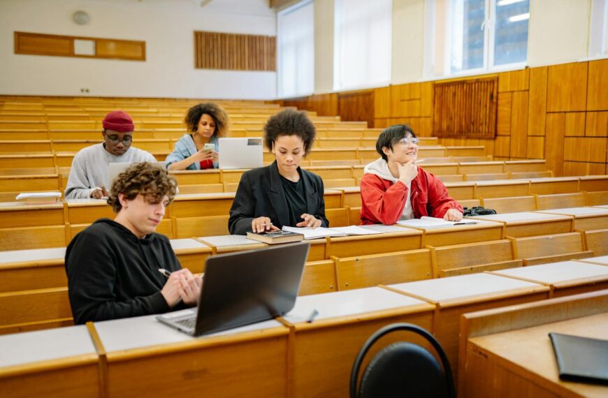 Group of college students studying together in a classroom, focused on learning with laptops and books.