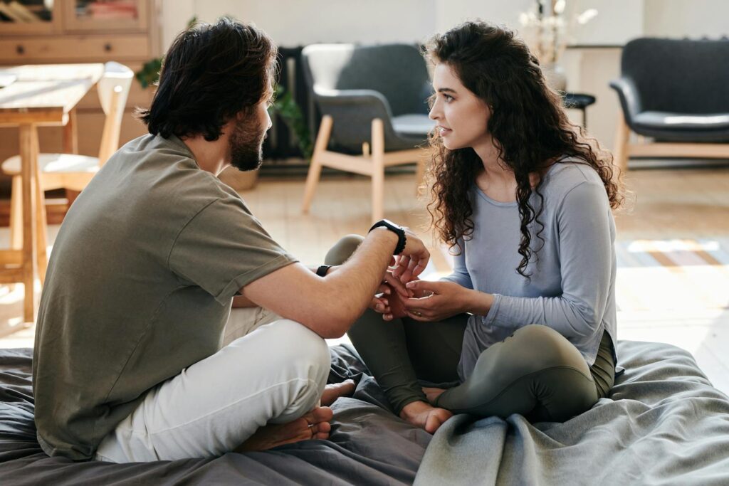 A couple sitting closely on a bed, engaged in a thoughtful discussion in a cozy home setting.