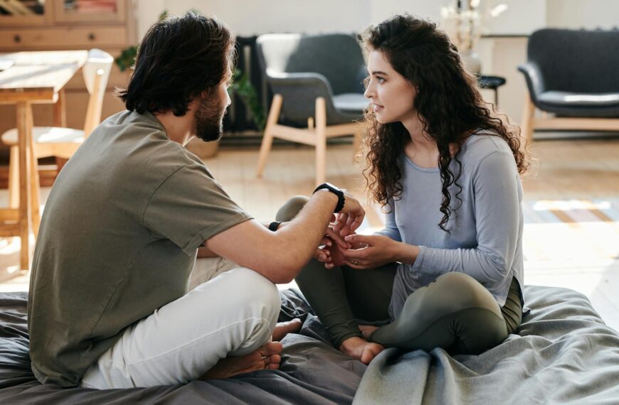 A couple sitting closely on a bed, engaged in a thoughtful discussion in a cozy home setting.