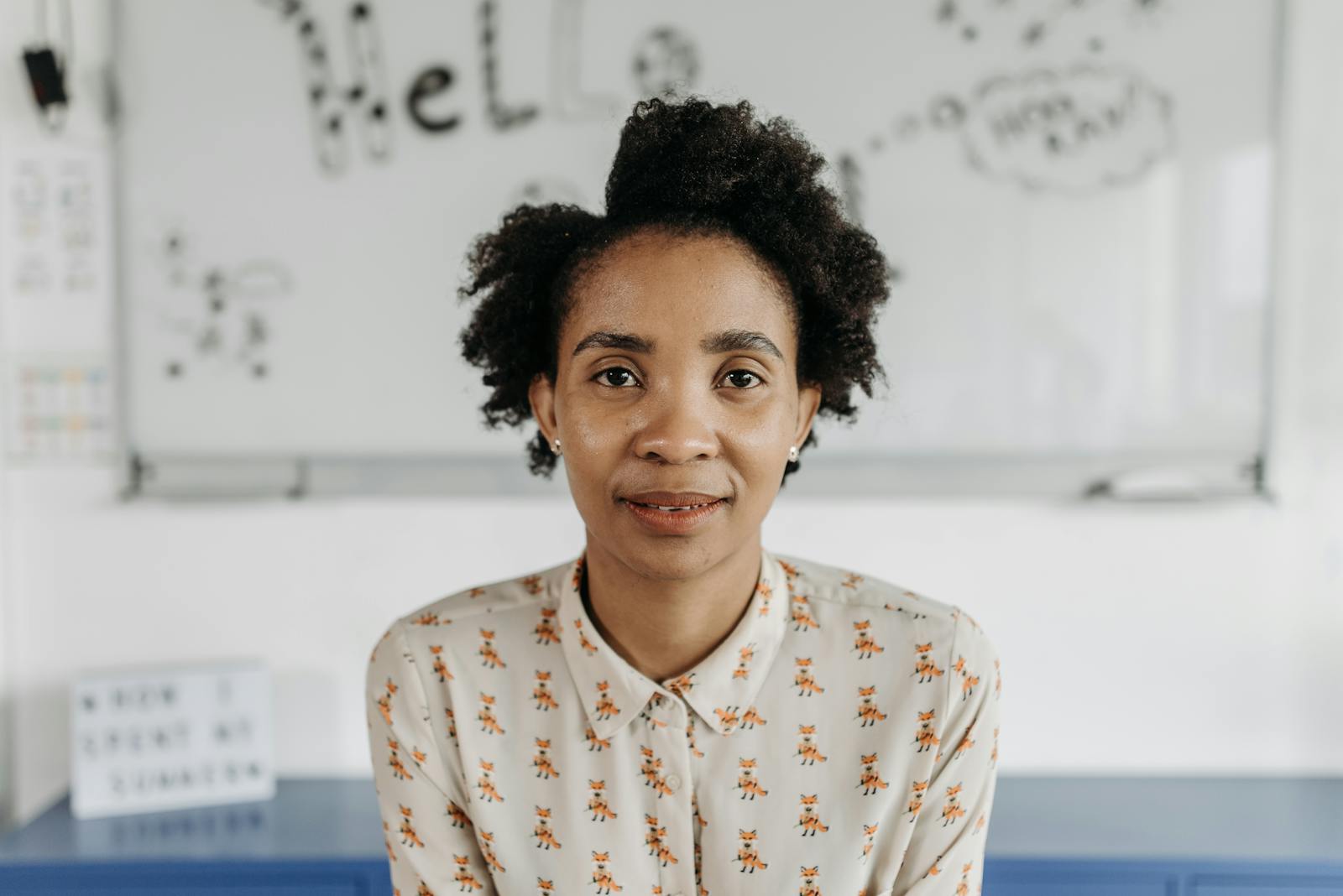 A confident woman with afro hair poses in a classroom, fostering an educational theme.
