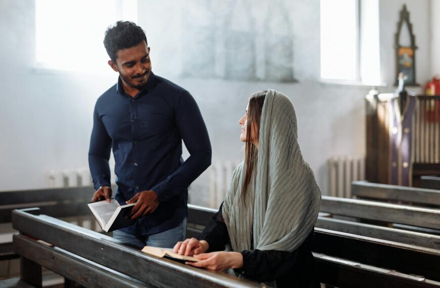 A South Asian man and woman seated in a church pew reading together, ambient light and peaceful setting.