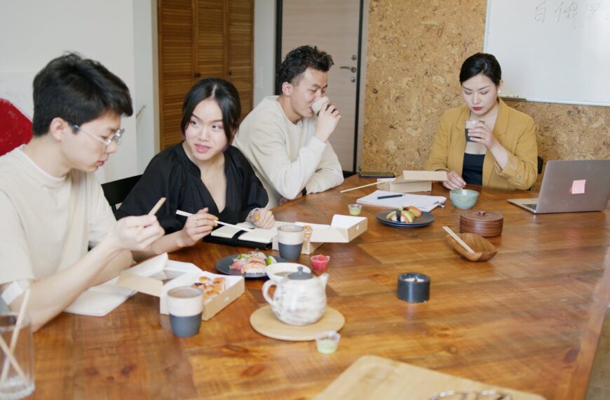 Team sharing sushi lunch around a wooden table in a contemporary office setting.