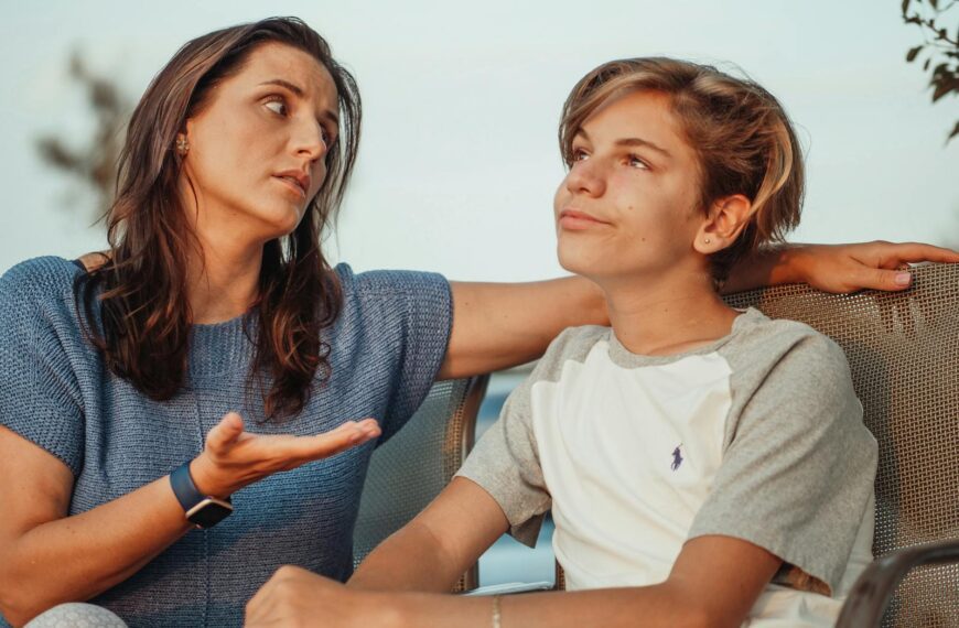 A mother and her teenage son engage in a conversation sitting outside, expressing familial warmth and connection.