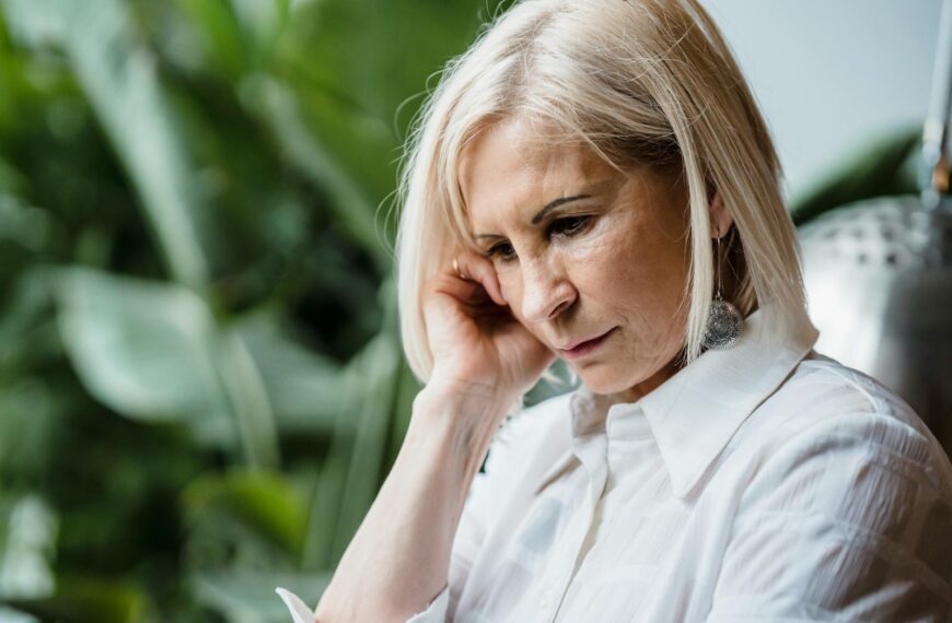 Senior woman in thoughtful pose surrounded by greenery indoors.