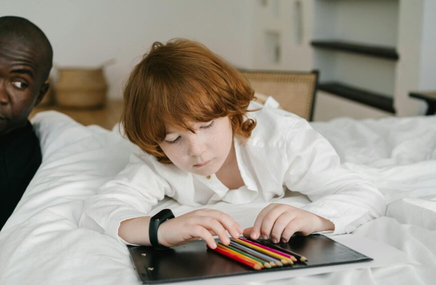 Red-haired child engaged in coloring with pencils on a bed indoors.