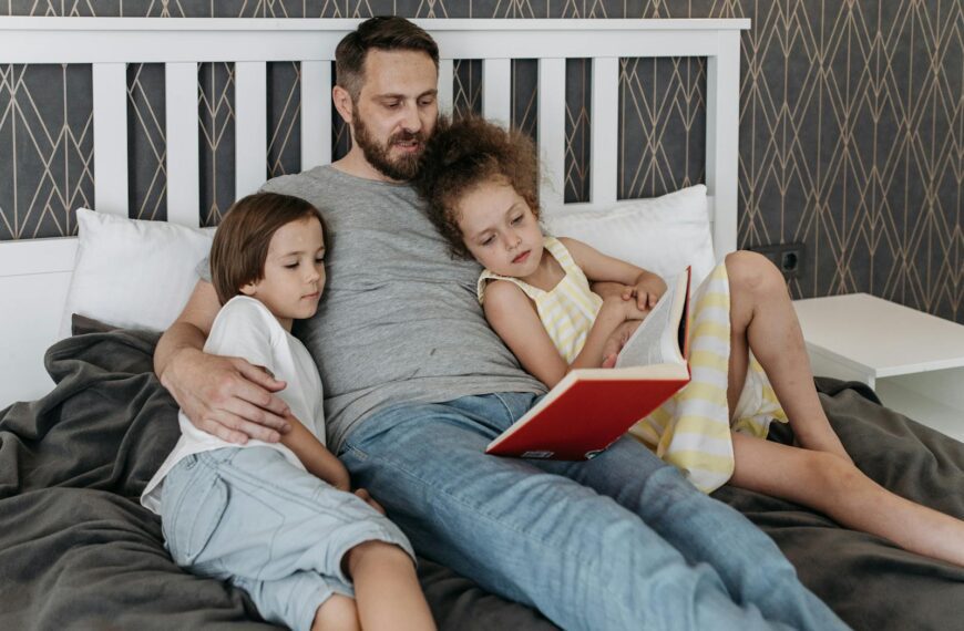 A father reads a storybook to his two children, creating a warm family moment in a cozy bedroom.