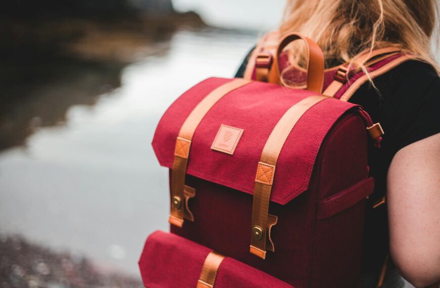 Close-up of a person with red backpack by a serene lakeside.