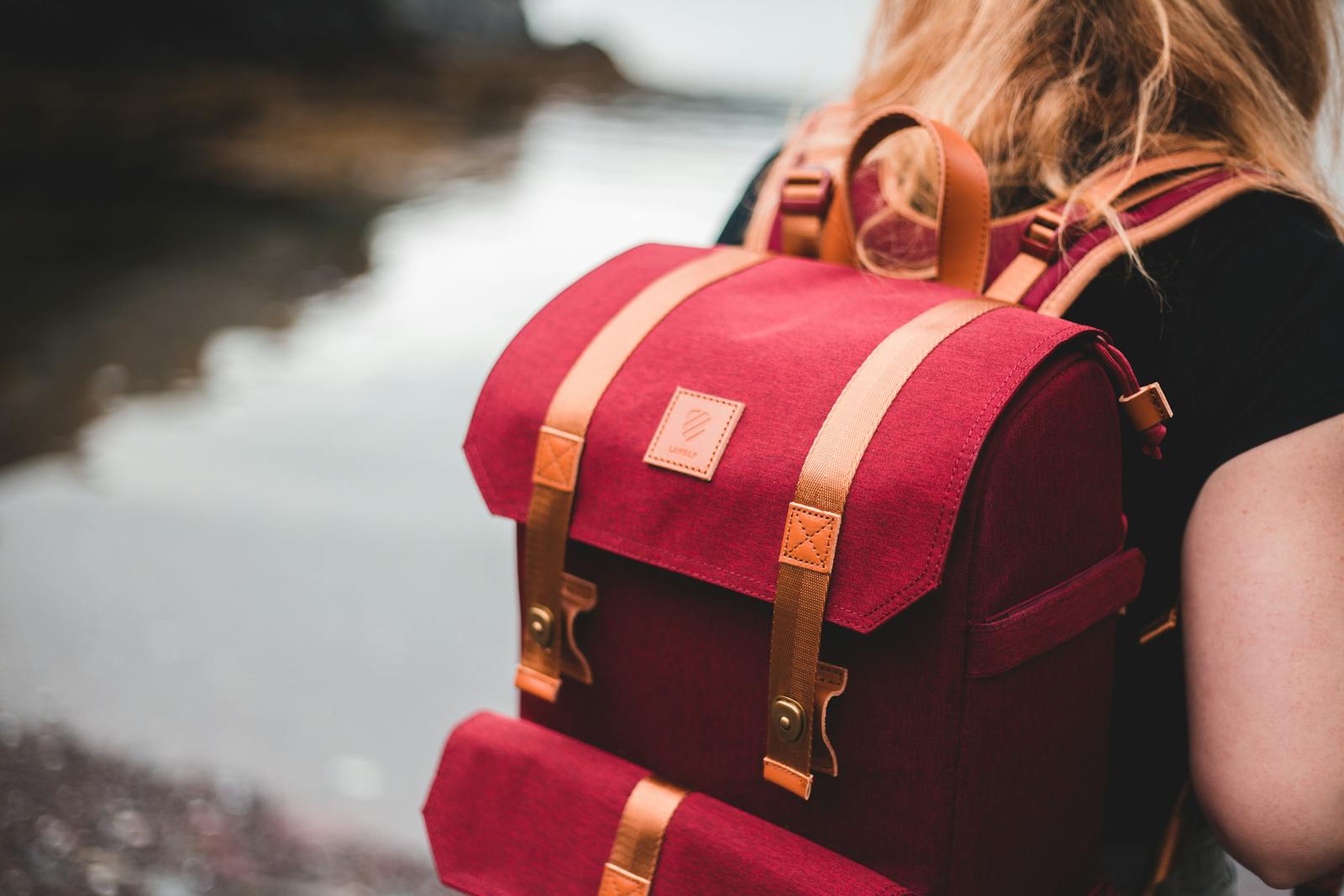 Close-up of a person with red backpack by a serene lakeside.
