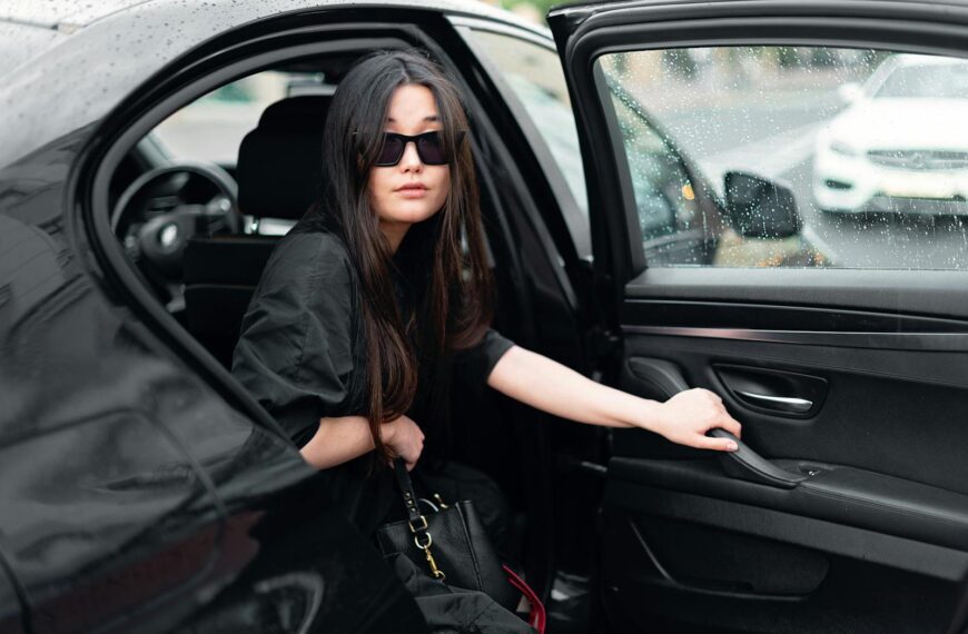 Stylish woman with sunglasses stepping out of a black luxury car in the rain.