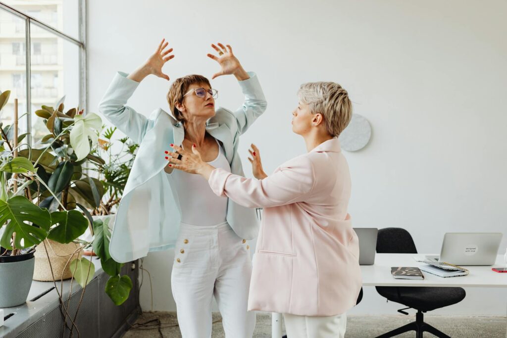 Two women in an office setting engaged in a vivid expression of ideas and emotion.