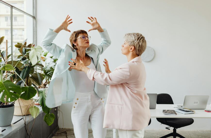 Two women in an office setting engaged in a vivid expression of ideas and emotion.