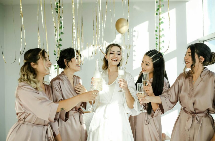 A group of bridesmaids in stylish robes celebrating with champagne indoors, creating a joyful and festive atmosphere.