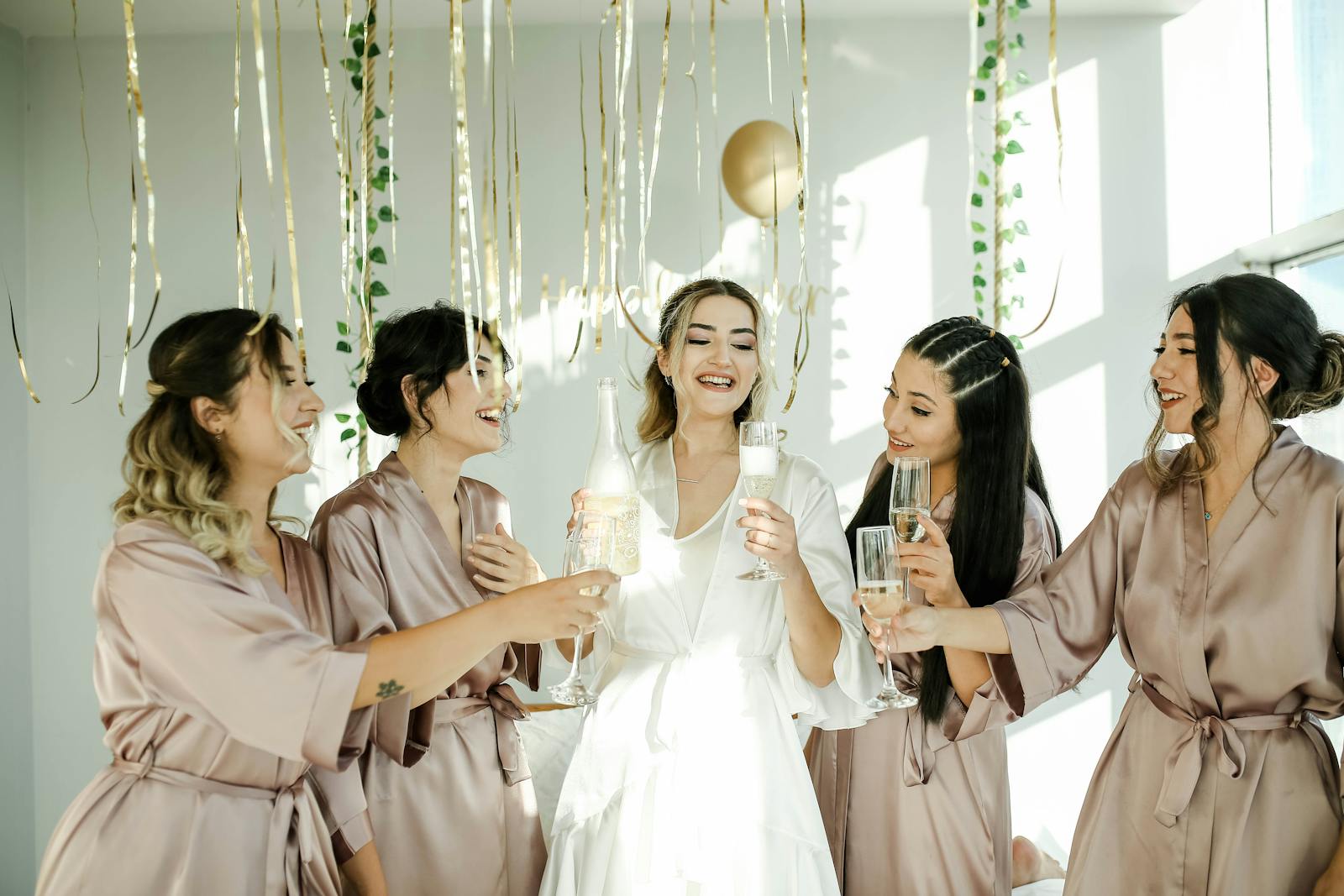 A group of bridesmaids in stylish robes celebrating with champagne indoors, creating a joyful and festive atmosphere.