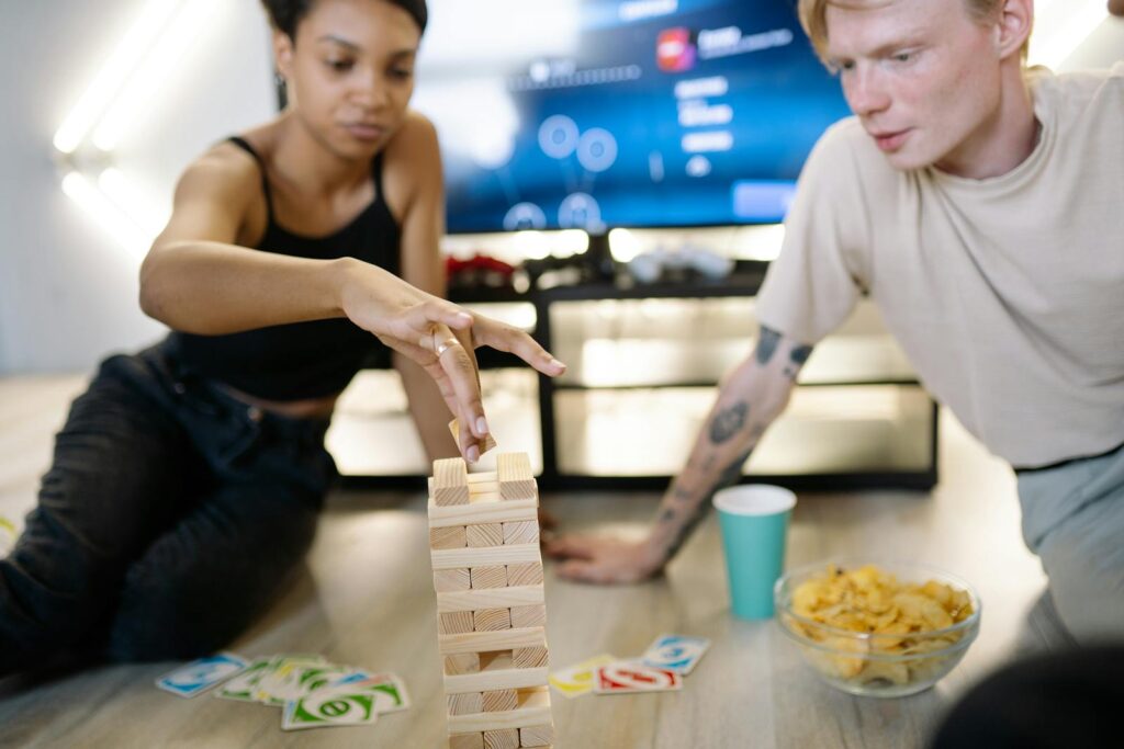 Two friends enjoying a fun game night with Jenga and cards indoors.