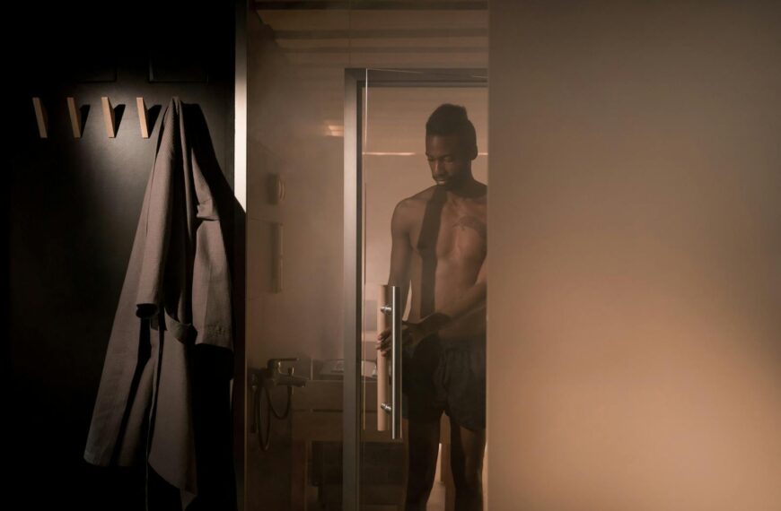 A shirtless man enters a steam-filled shower room, creating an intimate and relaxing atmosphere.