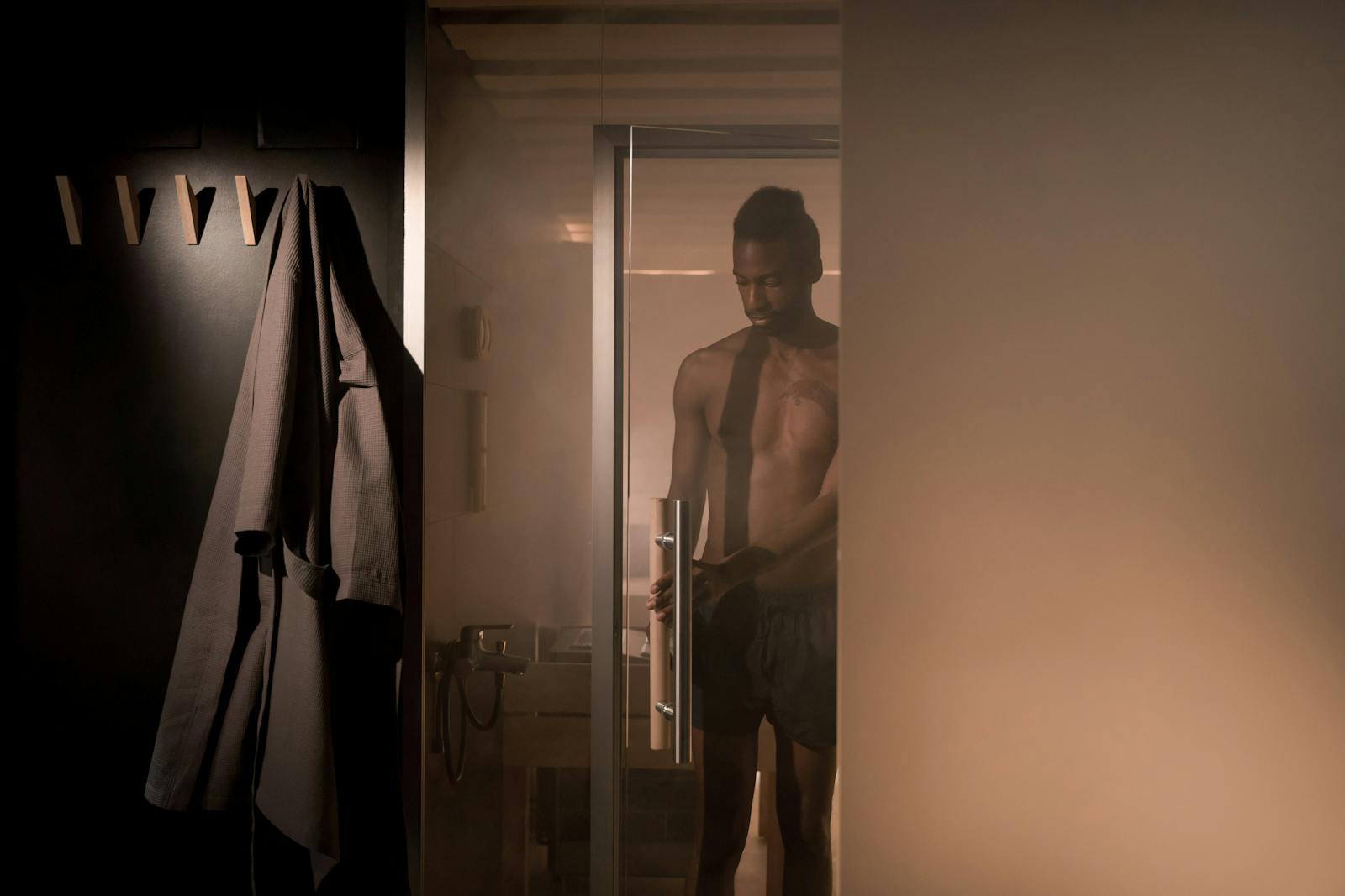 A shirtless man enters a steam-filled shower room, creating an intimate and relaxing atmosphere.