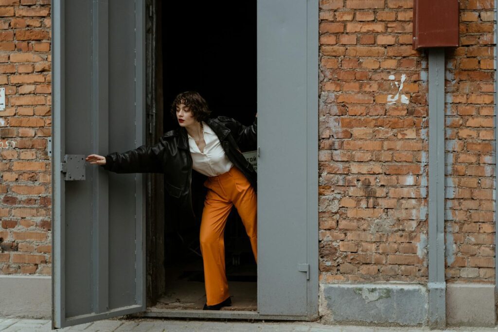 A woman in vibrant fashion opens a large industrial door set in a brick wall.