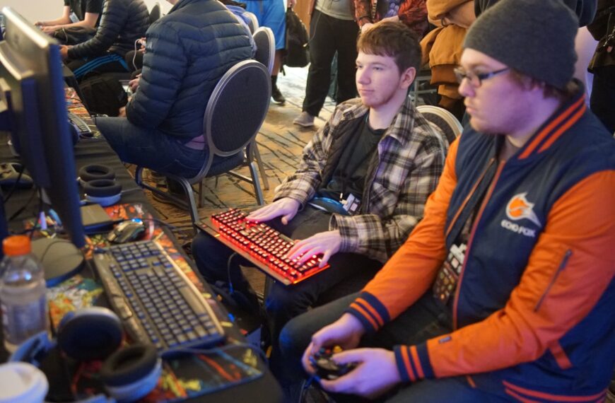 man using video game control pad beside man using computer keyboard sitting and playing video games