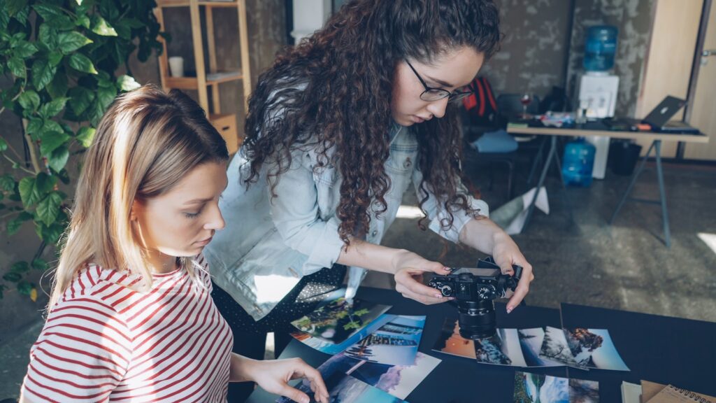 Two women examine photos at a table.