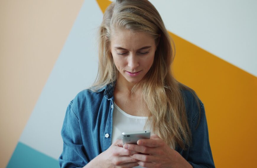 Young woman looking at her phone with a colorful wall.