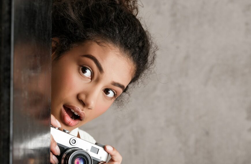 Young woman peeking around corner with camera