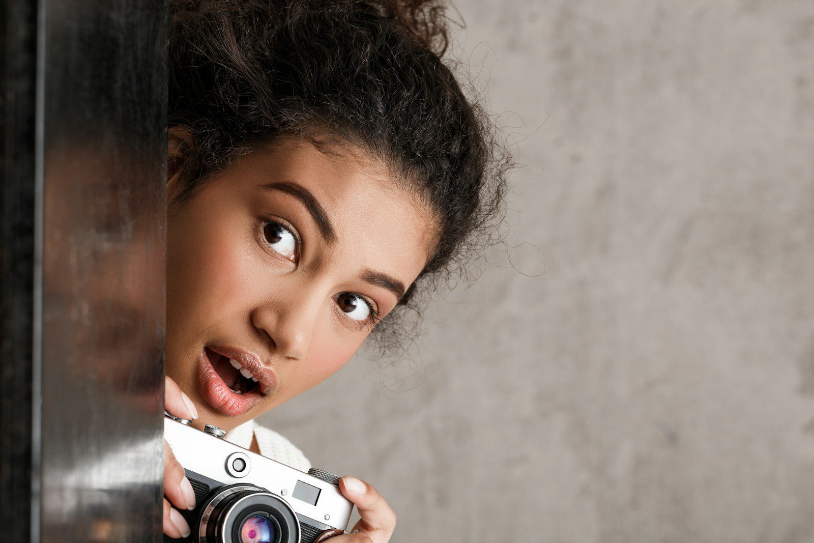 Young woman peeking around corner with camera