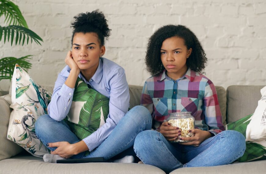 Two women sitting on a couch with popcorn.
